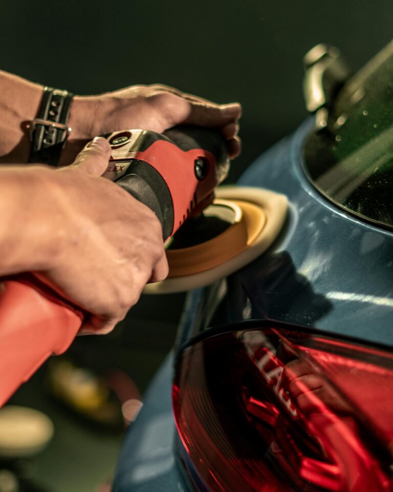 Hands using a buffing machine to polish a car for a glossy finish, highlighting car detailing process.