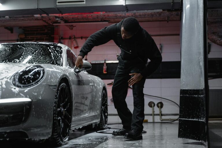 Man washing a luxury car in an indoor garage, emphasizing automotive care.