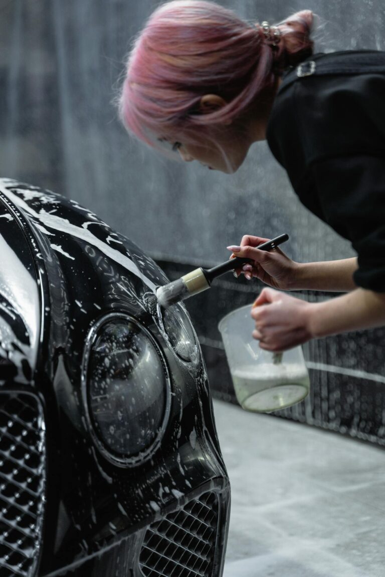 Woman cleaning car headlight with brush and soap at a car wash service.